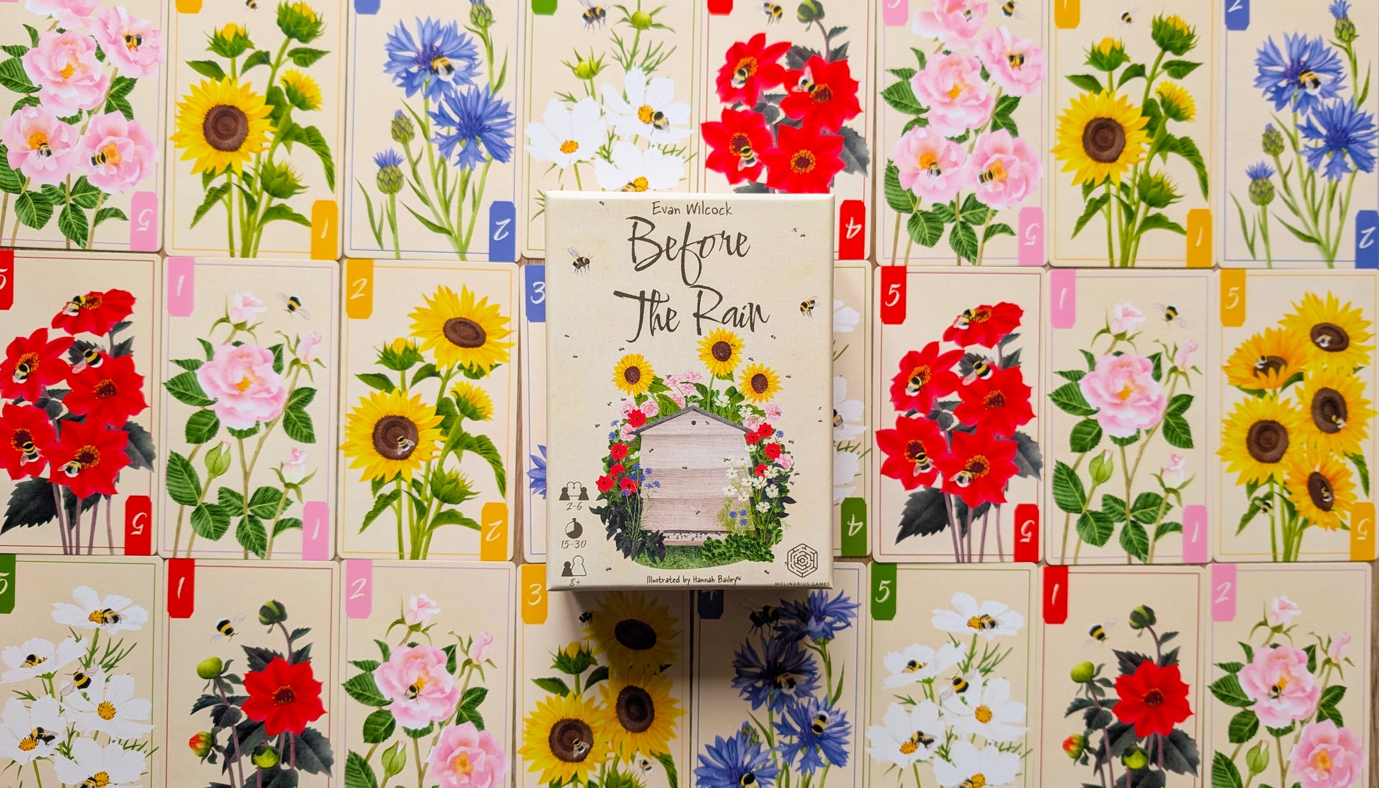 Game Box titled 'Before the Rain' surrounded by floral cards on a wooden surface