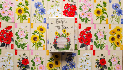Game Box titled 'Before the Rain' surrounded by floral cards on a wooden surface